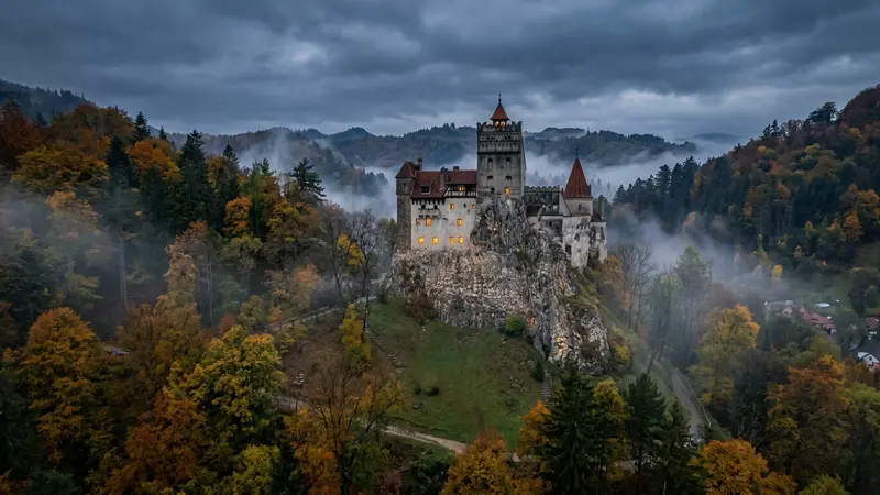 Castelo de Bran medieval erguido sobre colina rochosa cercado por florestas enevoadas de outono na Transilvânia, Romênia