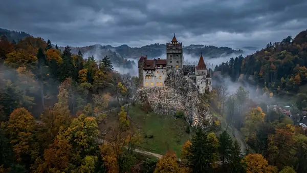 Castelo de Bran medieval erguido sobre colina rochosa cercado por florestas enevoadas de outono na Transilvânia, Romênia